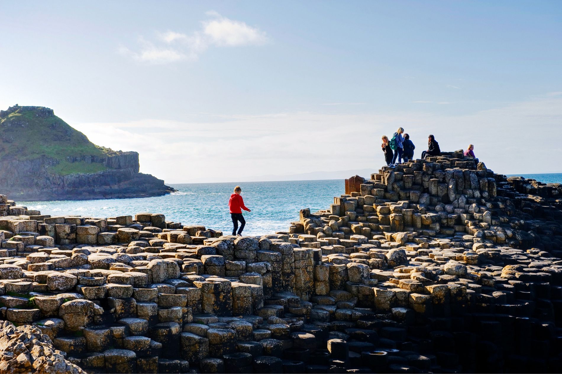 Dei turisti in visita alla costa della contea di Antrim esplorano le colonne di basalto della Giant’s Causeway sotto un cielo luminoso.